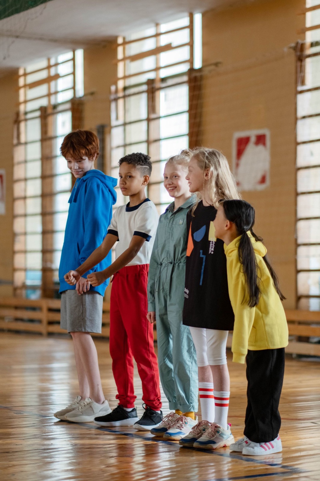 Primary school children lined up in a gym ready for a structured PE activity